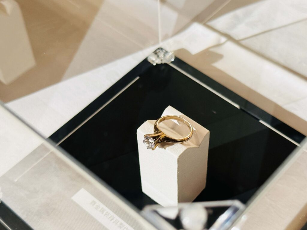Gold engagement ring with a large central diamond on a white display stand in a jewelry box.